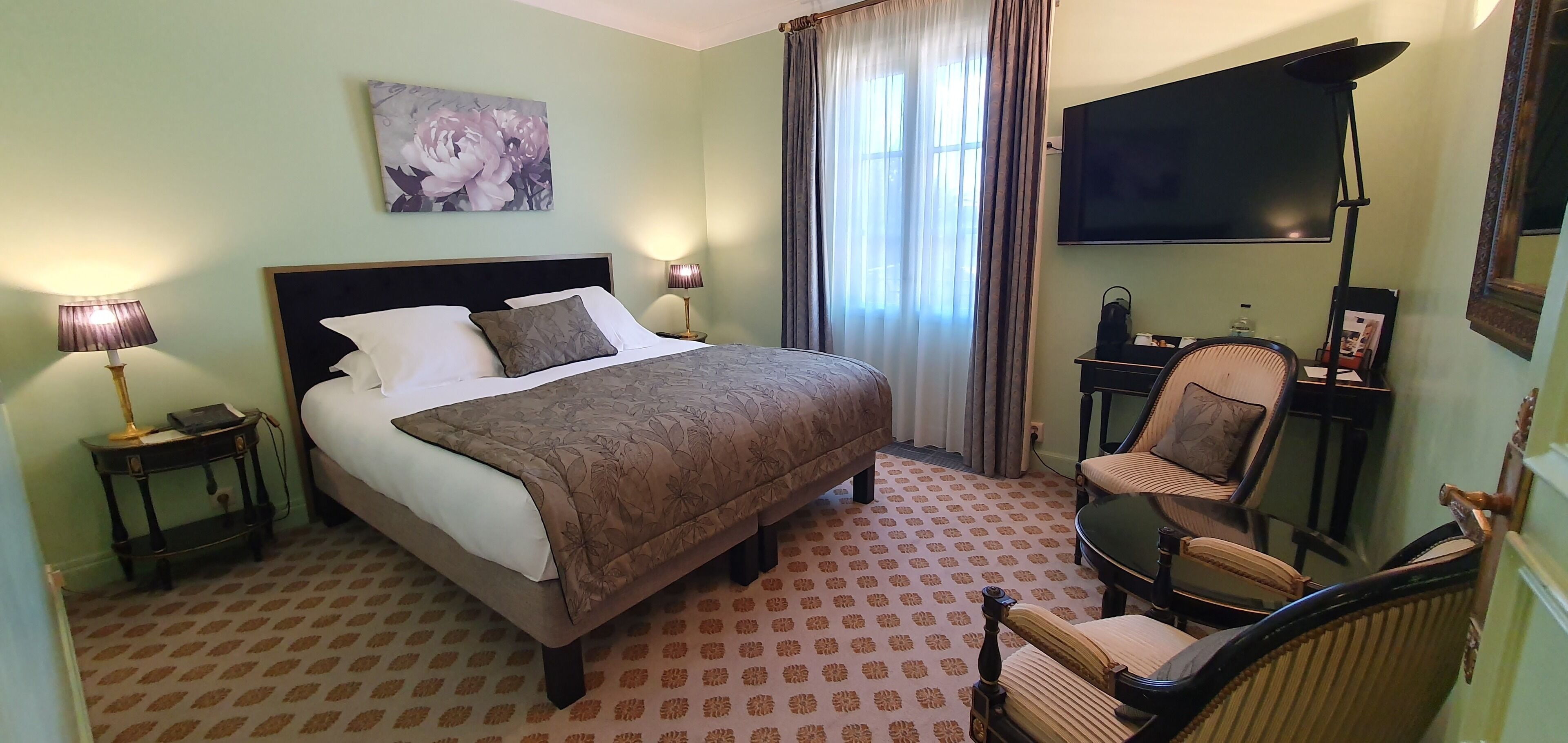 Habitación de hotel con una cama grande, una silla, un escritorio, un televisor y un cuadro en la pared.