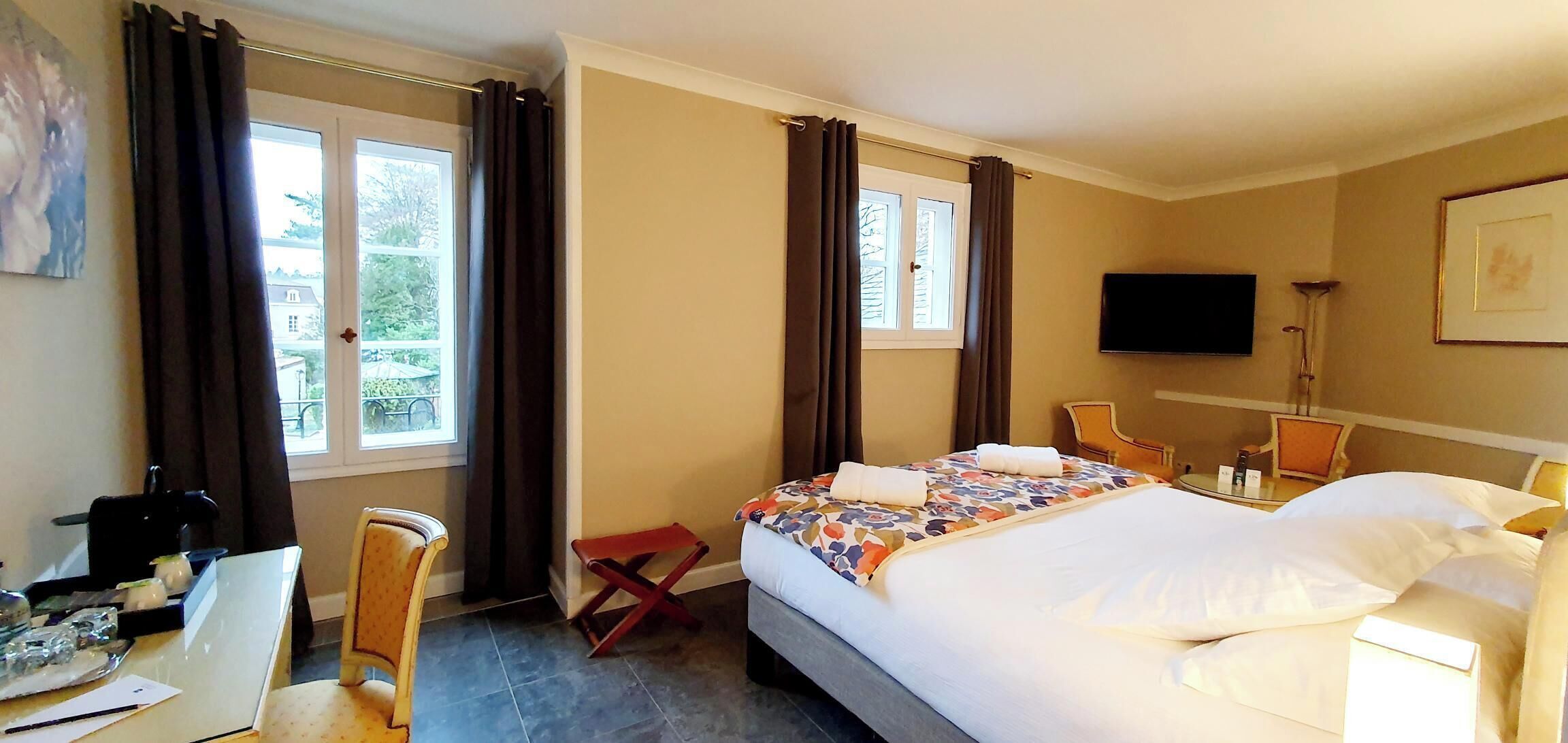 A hotel room with a bed, a desk, a chair, a TV, and a window with curtains.
