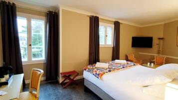 A hotel room with a bed, a desk, a chair, a TV, and a window with curtains.
