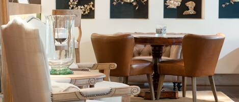 A dining area with a round table and four brown chairs. There are framed artworks on the wall behind the table.