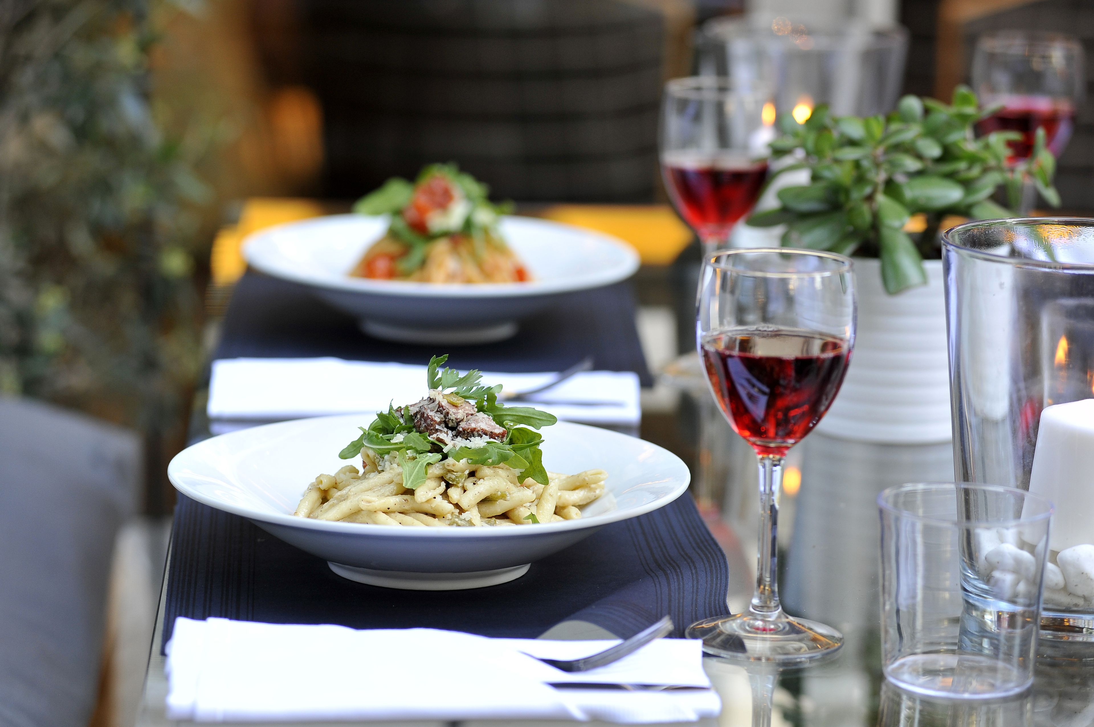 A dining table set with plates of pasta, wine glasses, and a vase with flowers.