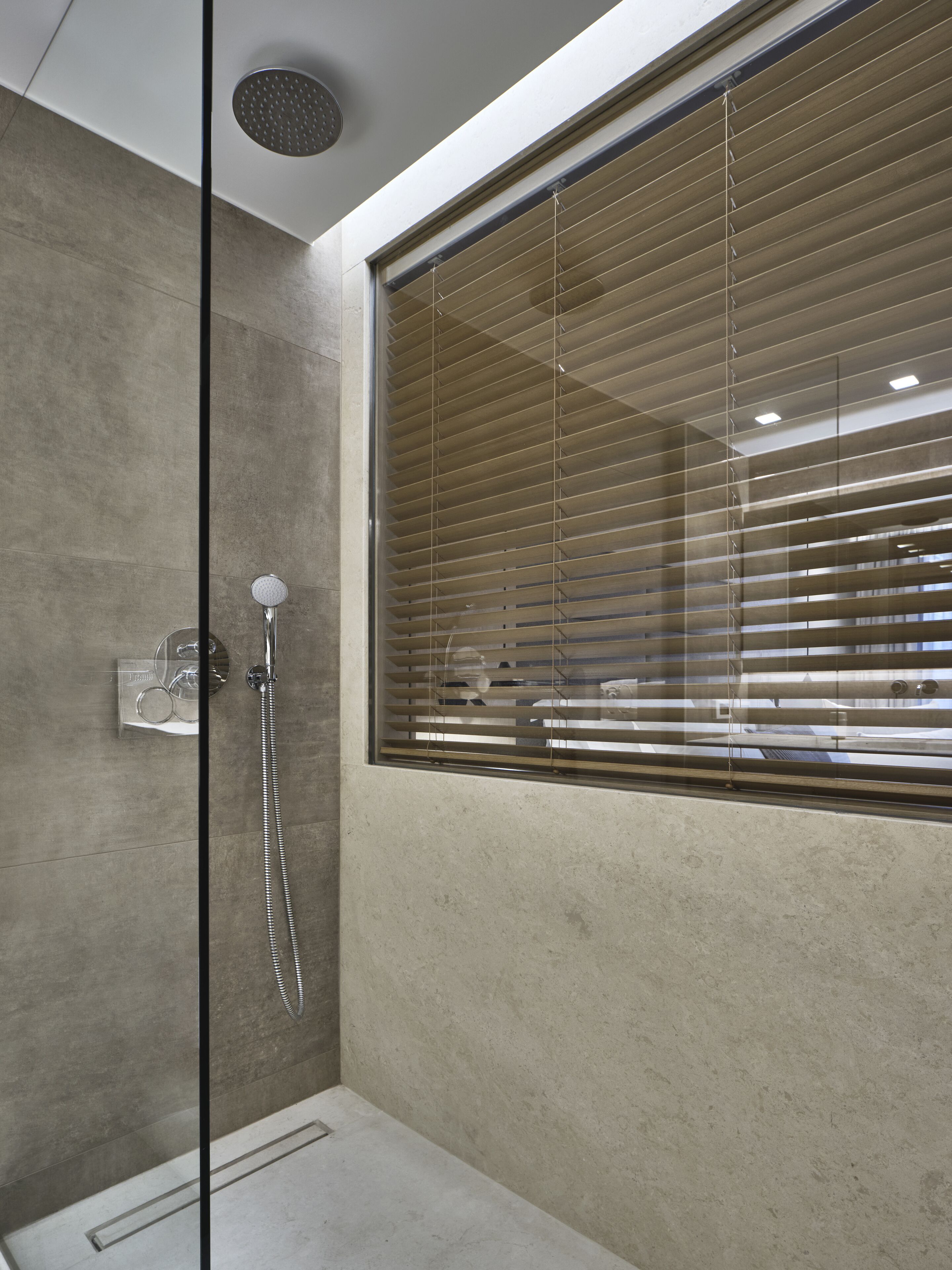 Een moderne badkamer met een douchecabine van glas, een inbouwtoilet en een raam met zonwering.