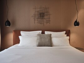 Una cama bien tendida con ropa de cama blanca y gris, cabecera marrón y dos lámparas colgantes negras.