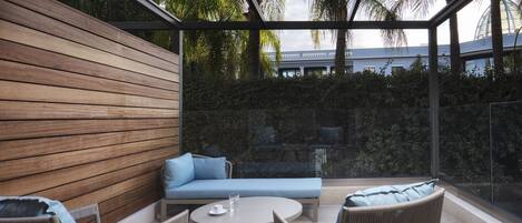 Un espacio exterior moderno con mobiliario de madera, sillas de mimbre y una mesa redonda.