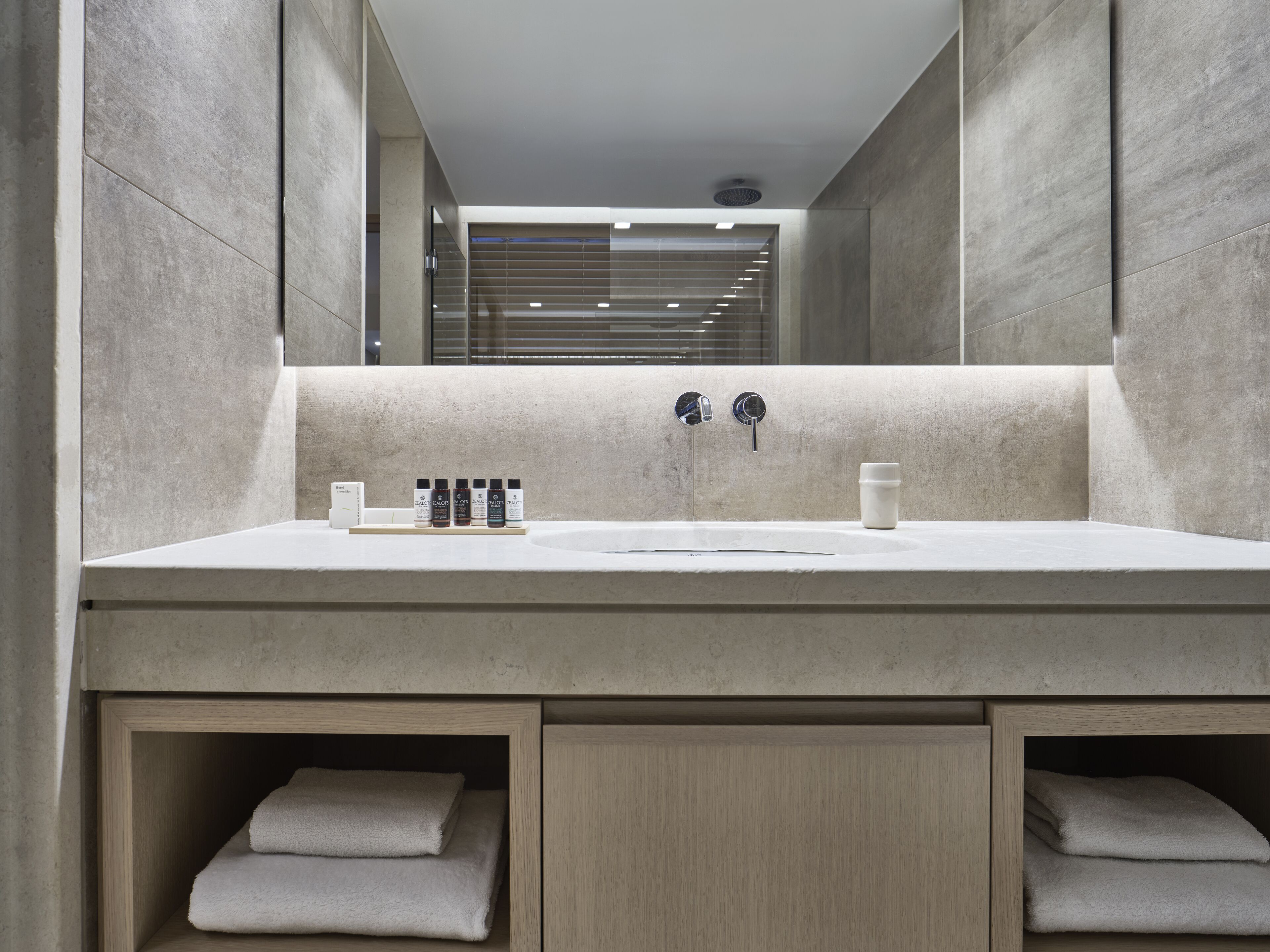Une salle de bain moderne avec un grand lavabo, deux robinets et un miroir. On y trouve des articles de toilette sur le lavabo et des serviettes rangées dans des armoires en bois situées en dessous.