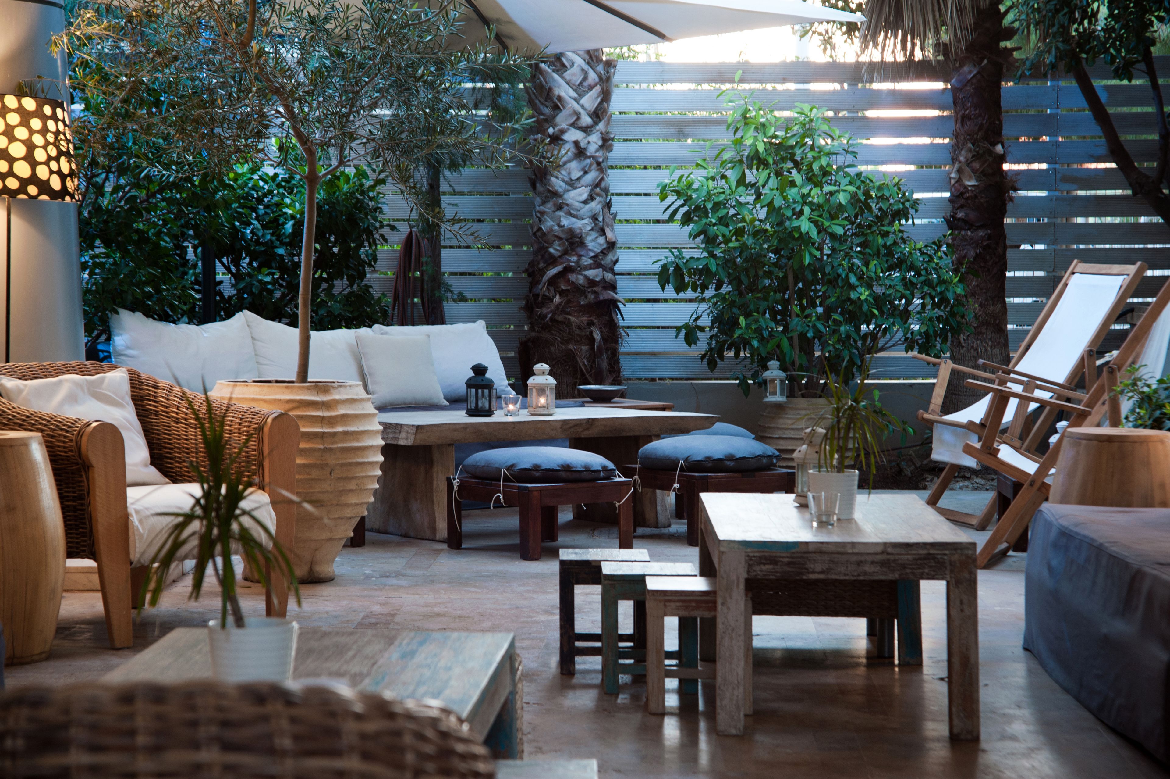 Un patio al aire libre con mobiliario de mimbre, mesas de madera y plantas en macetas.