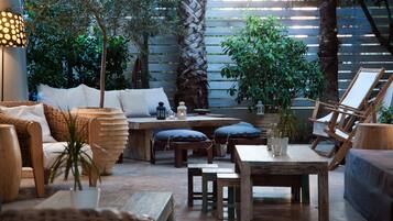 Un patio al aire libre con mobiliario de mimbre, mesas de madera y plantas en macetas.