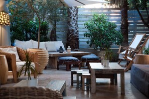 An outdoor patio area with wicker furniture, wooden tables, and potted plants.