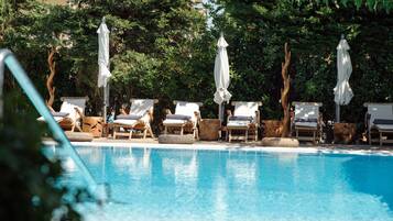 Un área junto a la piscina con sillones de descanso y sombrillas.