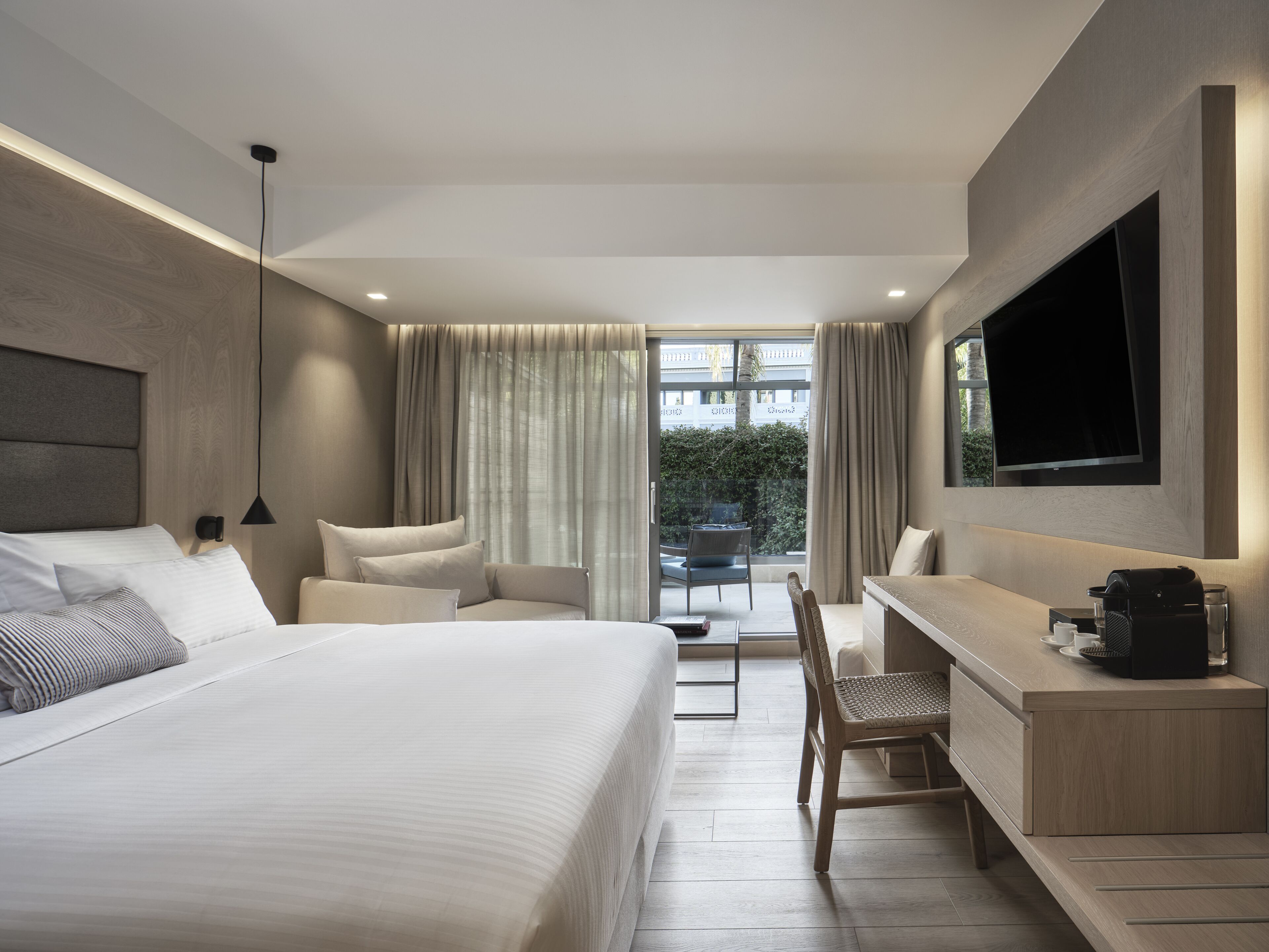 Una habitación de hotel moderna con una cama grande, un escritorio, una silla, un televisor y un balcón con cortinas.