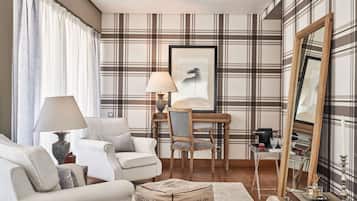 Una sala de estar con papel tapiz escocés, una silla de madera, un sofá blanco, una mesa con una lámpara y un espejo.