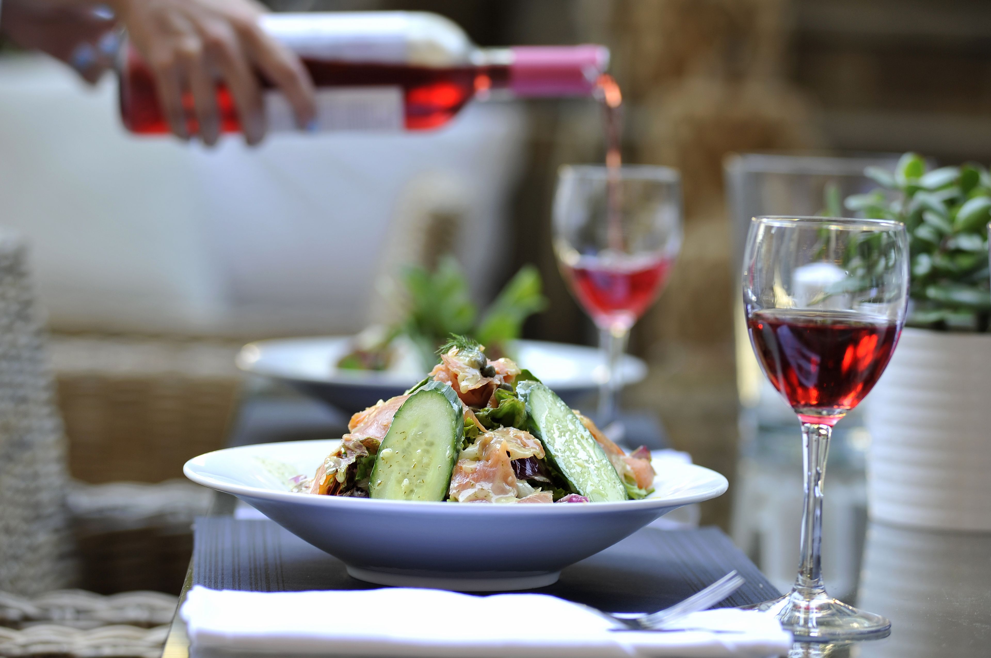 A table with a salad, a glass of red wine, and a bottle being poured.