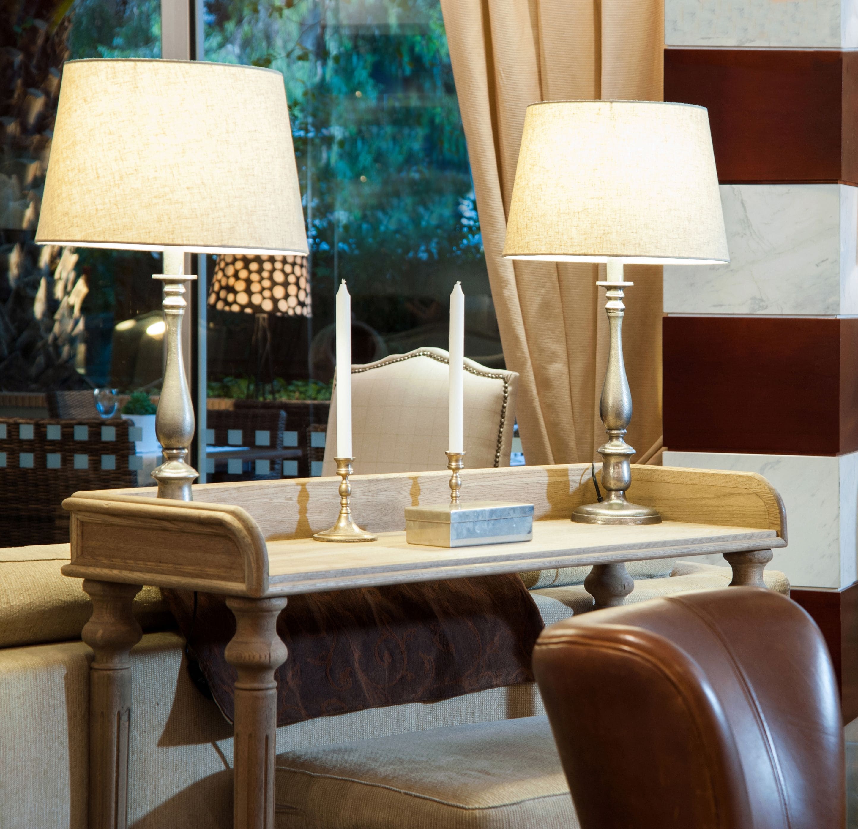 A well-lit room with a wooden table, two lamps, a candle, and a chair.
