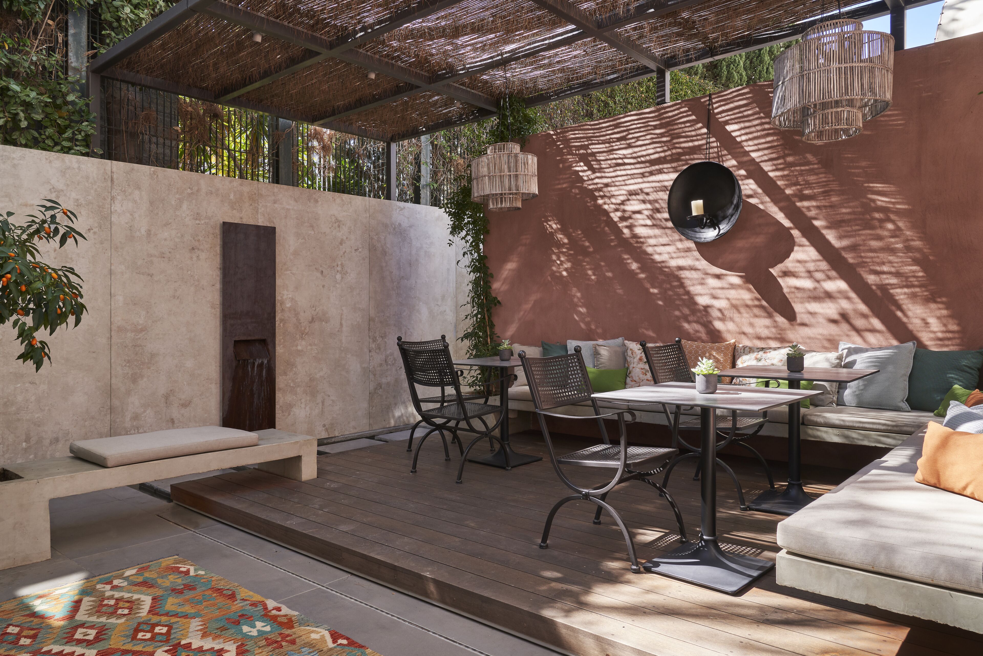 Eine Terrasse im Freien mit Holzdeck, einer Sitzecke mit Sofa und Sesseln, einem kleinen Tisch und einer hängenden Leuchte.