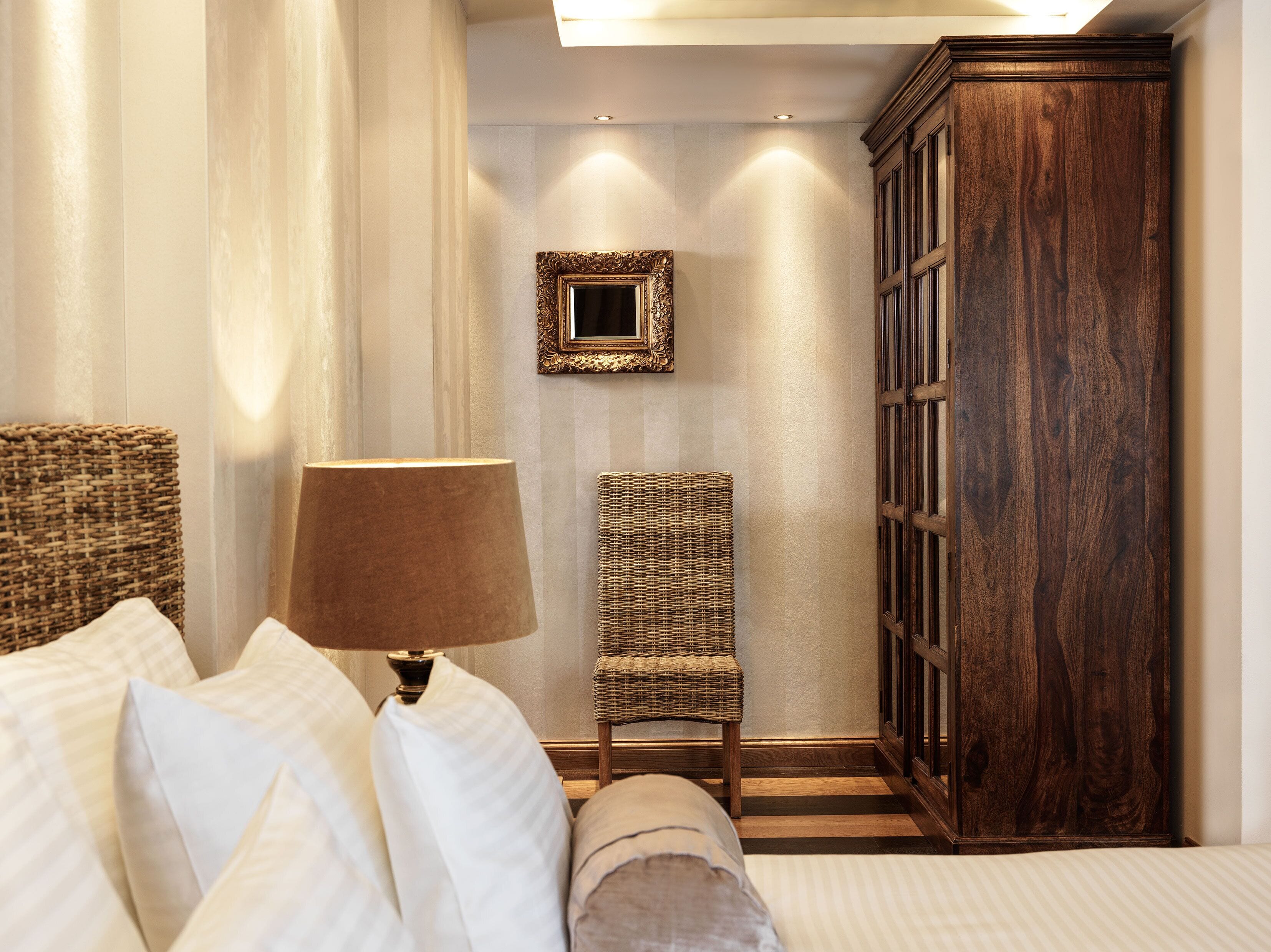 A bedroom with a bed, a lamp, a wicker chair, and a wooden cabinet.
