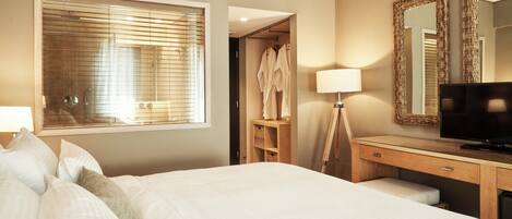 A hotel room with a large bed, a television, a desk with a lamp, a wardrobe, and a mirror.
