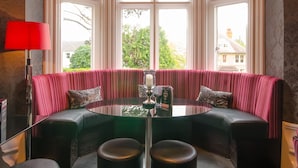 A room with a large bay window, a round table, and a red lamp. - Cotford Hotel (Malvern)