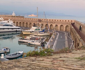 A marina with boats docked, a stone bridge, and a view of the sea.