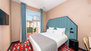 Een hotelkamer met een groot bed, een aan de muur bevestigde televisie, een raam met gordijnen en een kamerbreed tapijt met een patroon.