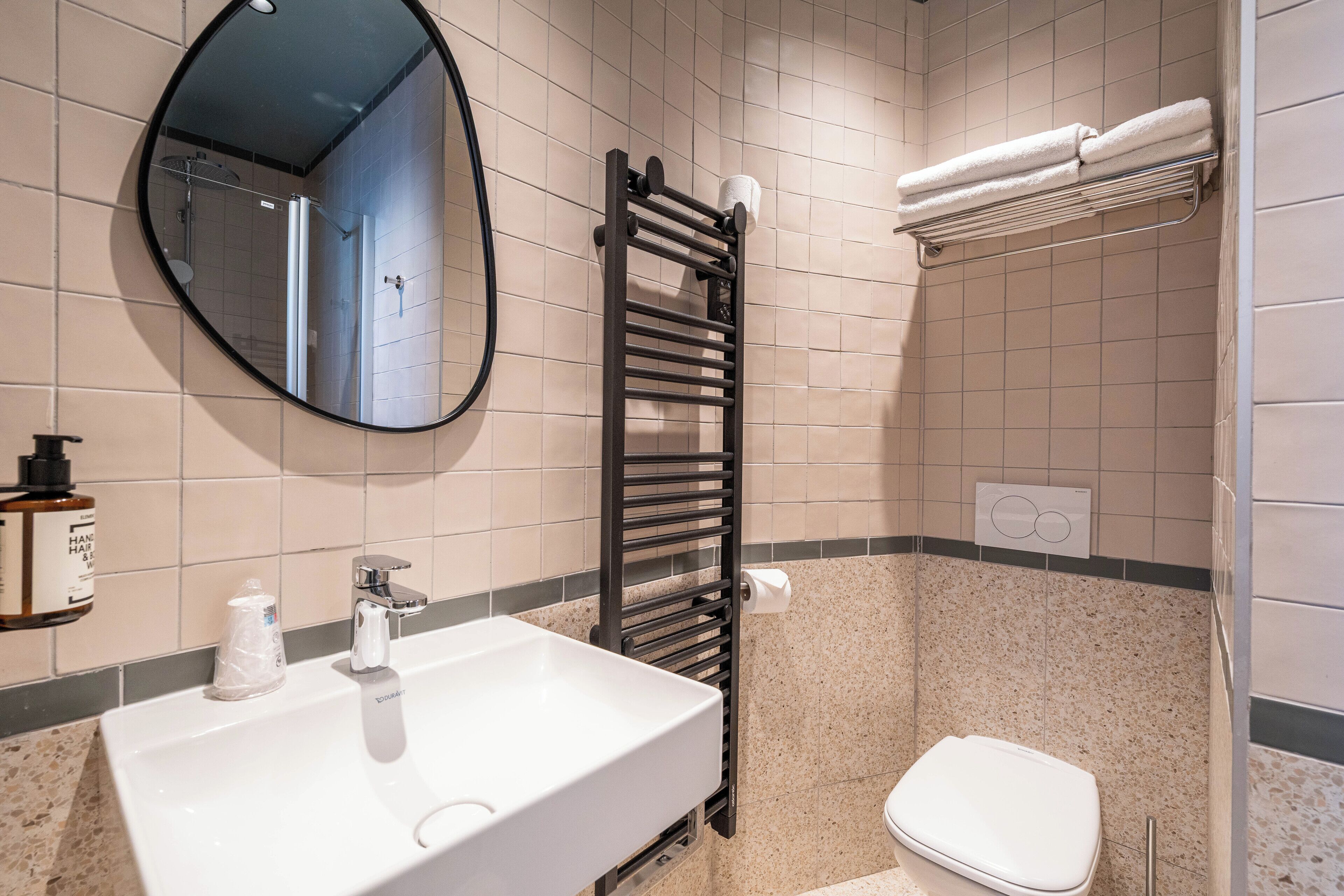 A bathroom with a white sink, a black towel rack, a toilet, and a mirror.