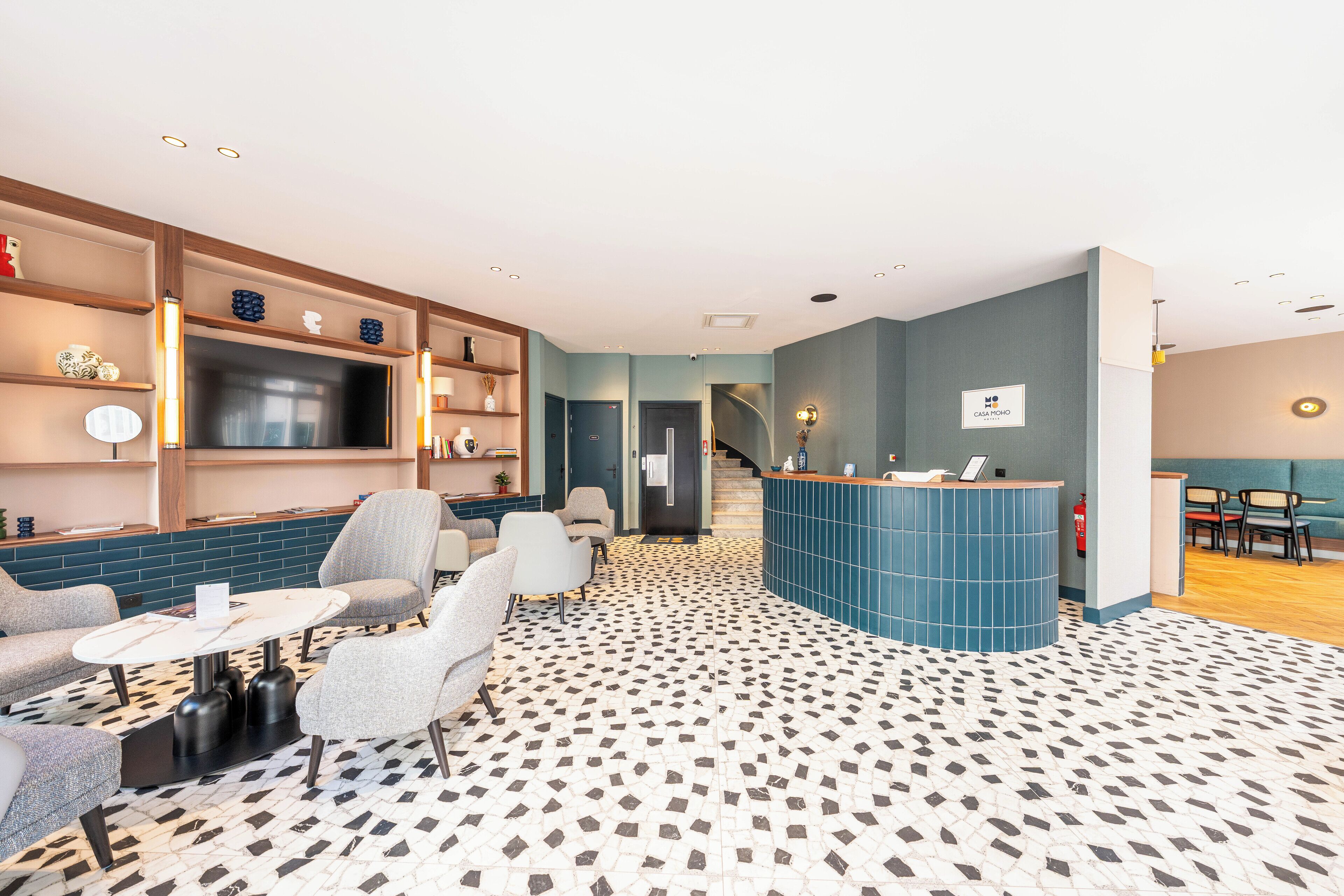 A modern hotel lobby with a reception desk, seating area, and a patterned floor.