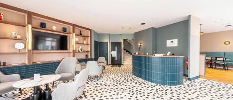 A modern hotel lobby with a reception desk, seating area, and a patterned floor.