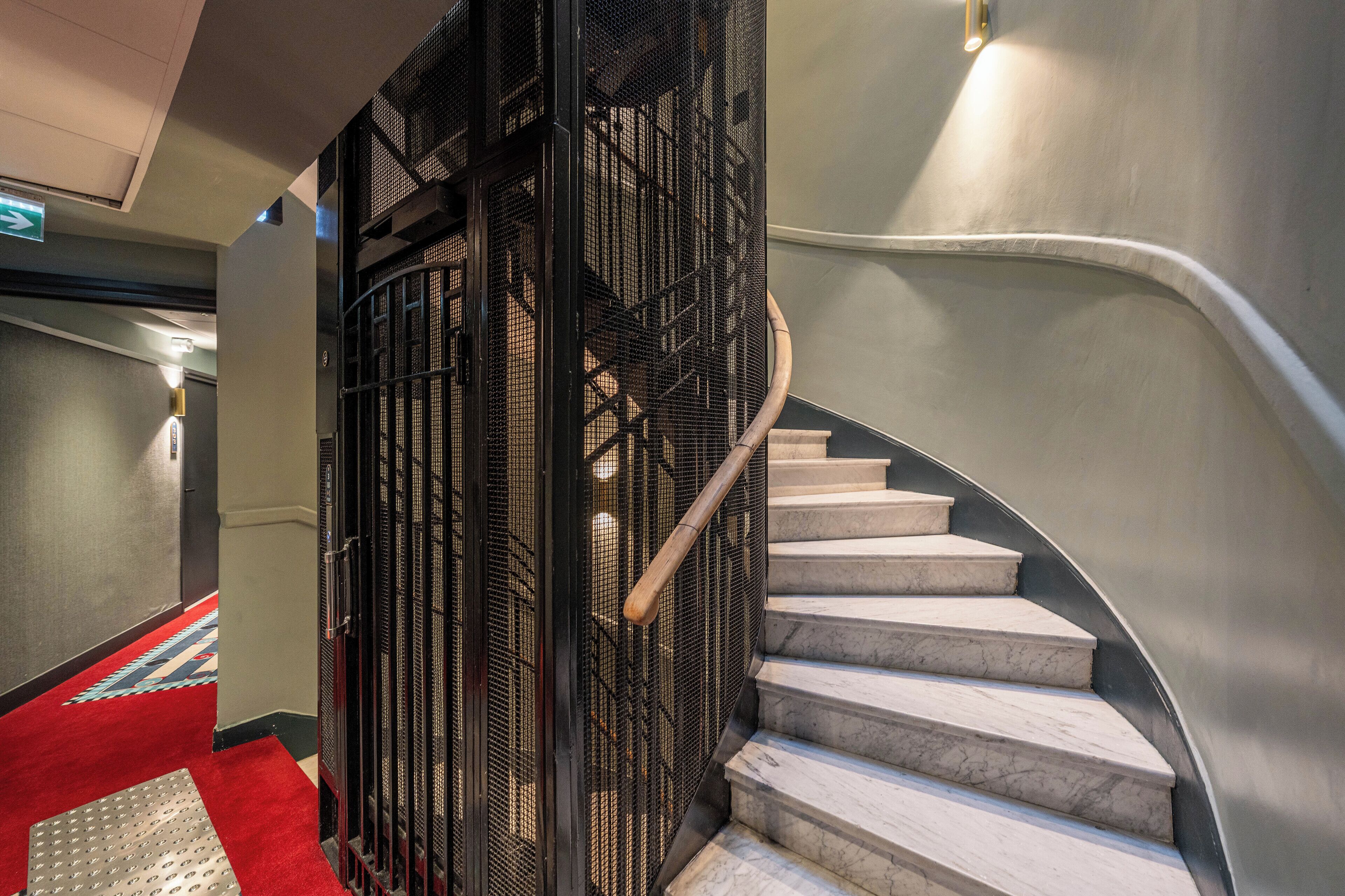 Eine geschwungene Treppe mit Metallgeländer, einem mit rotem Teppich ausgelegten Bereich und einer strukturierten Fußmatte.