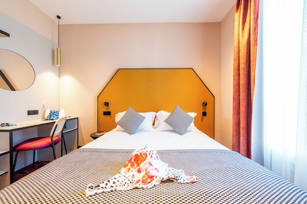 A hotel room with a large bed, a desk with a chair, a mirror, and a window with curtains.