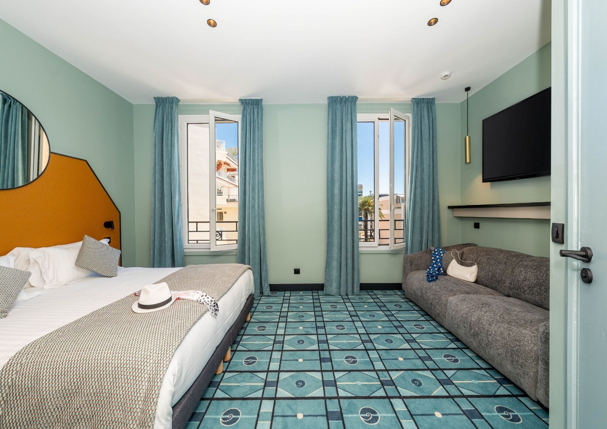A hotel room with a bed, a sofa, a TV, and a patterned floor.