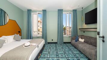 A hotel room with a bed, a sofa, a TV, and a patterned floor.