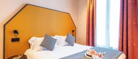 A hotel room with a large bed, a side table, and a window with curtains.