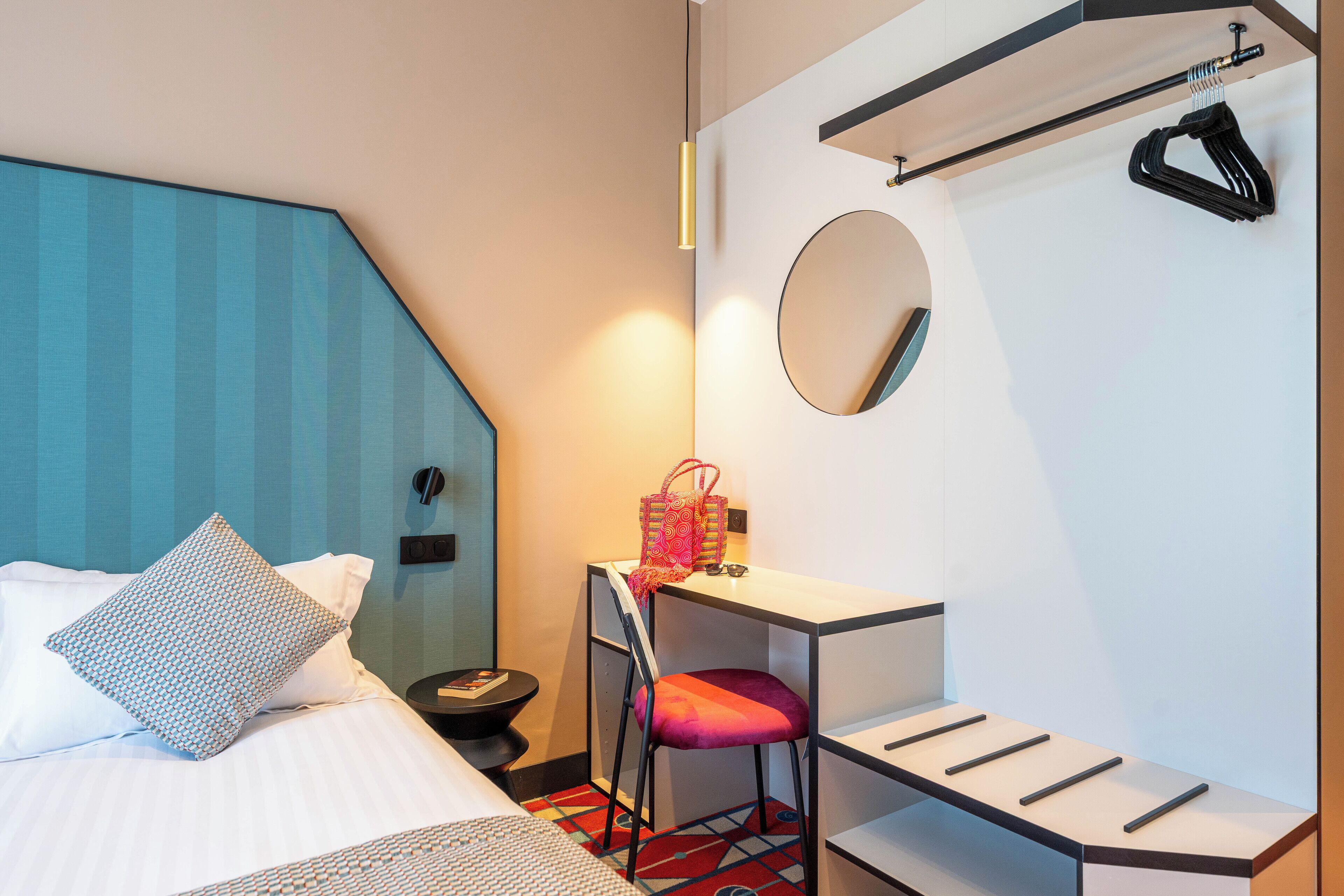 Een hotelkamer met een bed, een bureau, een stoel, een klein tafeltje, een spiegel en een kapstok.