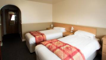 Habitación de hotel con dos camas, cada una con una mesita de noche y una lámpara. Se ve una puerta que conduce a otra habitación y una silla en la esquina.