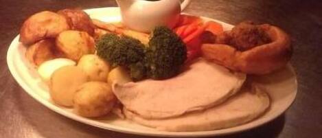 A plate with roast beef, Yorkshire pudding, vegetables, and gravy.