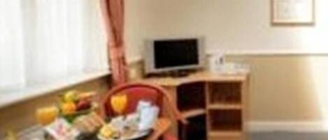 Quarto com mesa de jantar posta para dois, televisão em móvel e quadro na parede.