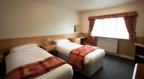 Habitación de hotel con dos camas, un escritorio, una silla, un espejo y una ventana con cortinas.