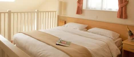 A neatly made bed with a magazine, a wooden headboard, a nightstand, and a window with curtains.