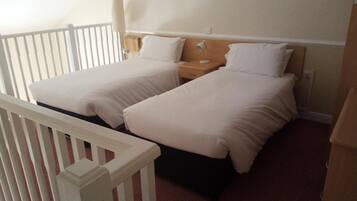 A bedroom with two beds, a nightstand, a lamp, and a white railing.