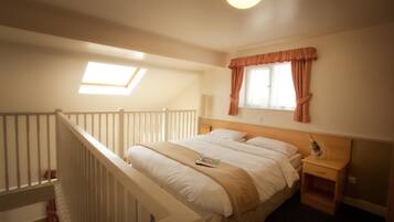 A hotel room with a large bed, a nightstand, a window with curtains, a skylight, and a staircase.