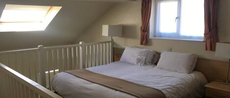 Un dormitorio con una cama individual, una mesita de noche, una lámpara, una ventana con cortinas y un tragaluz.