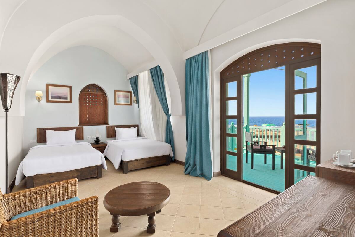 Ein Hotelzimmer mit zwei Betten, einem Balkon mit Aussicht und einem Essbereich.