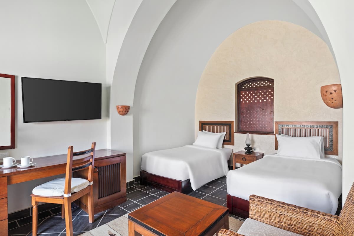 Ein Hotelzimmer mit zwei Betten, einem Schreibtisch mit Stühlen, einem Fernseher und einer Wanddekoration.