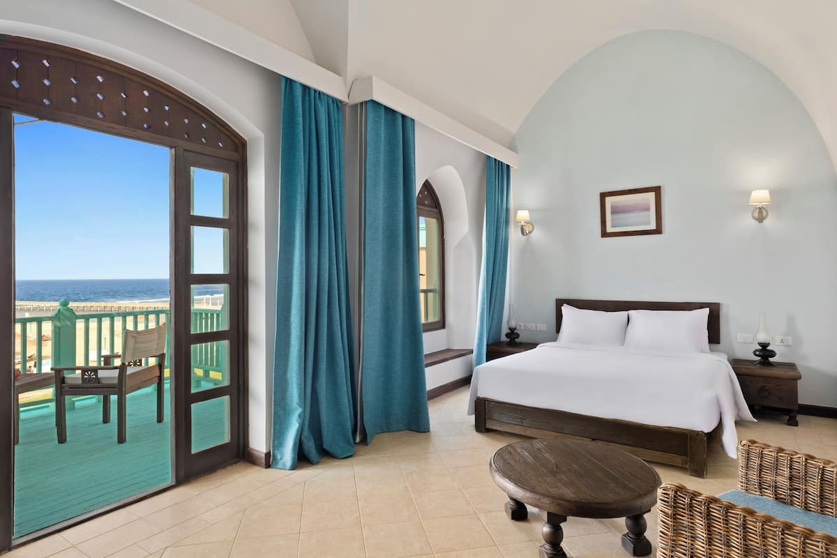 Ein Hotelzimmer mit Balkon, einem Bett, einem Nachttisch und Blick aufs Meer.