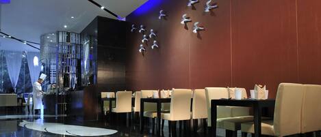 A modern restaurant with a chef preparing food, a wall with bird sculptures, and a polished floor.