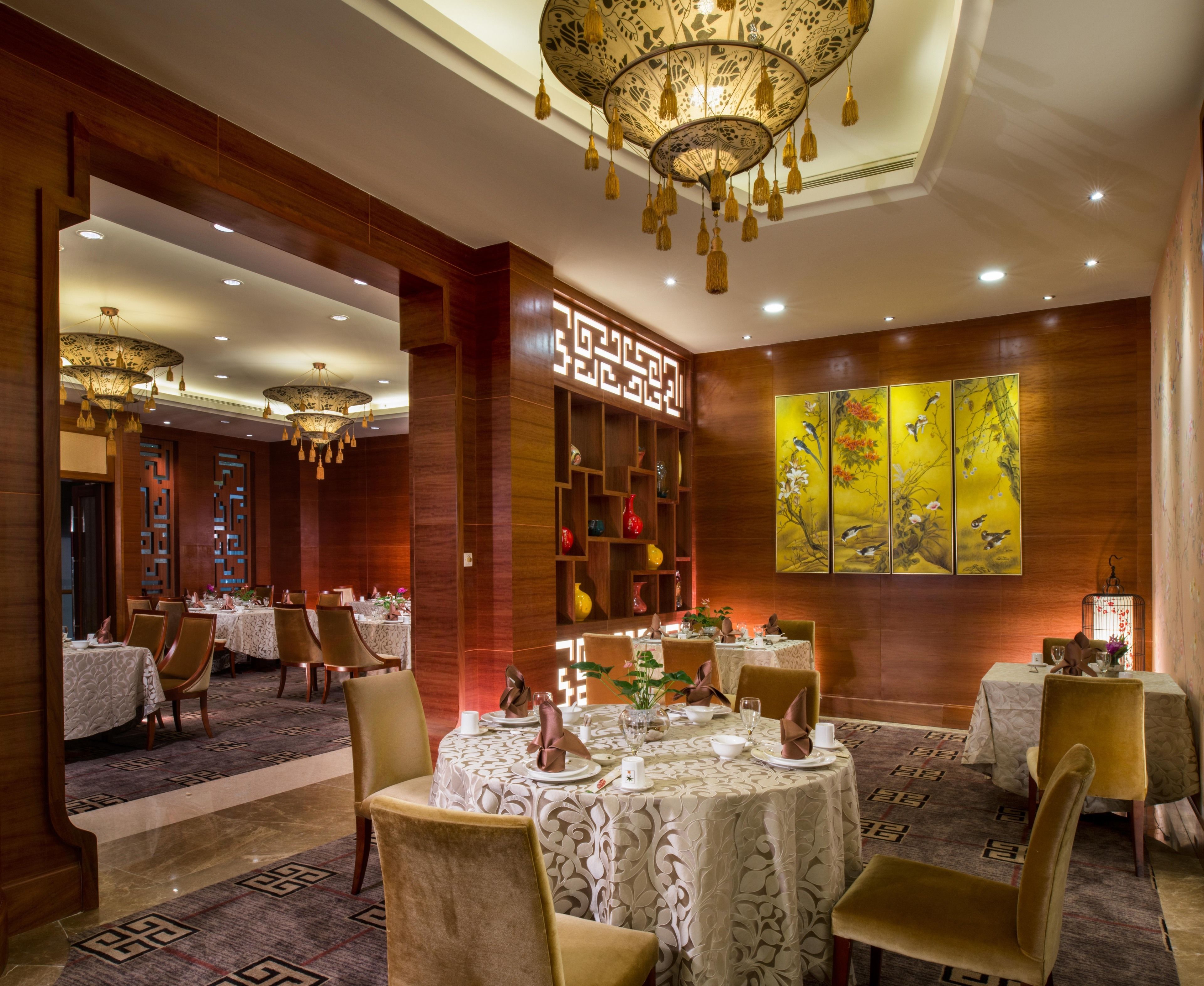 Un comedor bien iluminado con mesas redondas, sillas y una pared decorativa con una pintura floral.