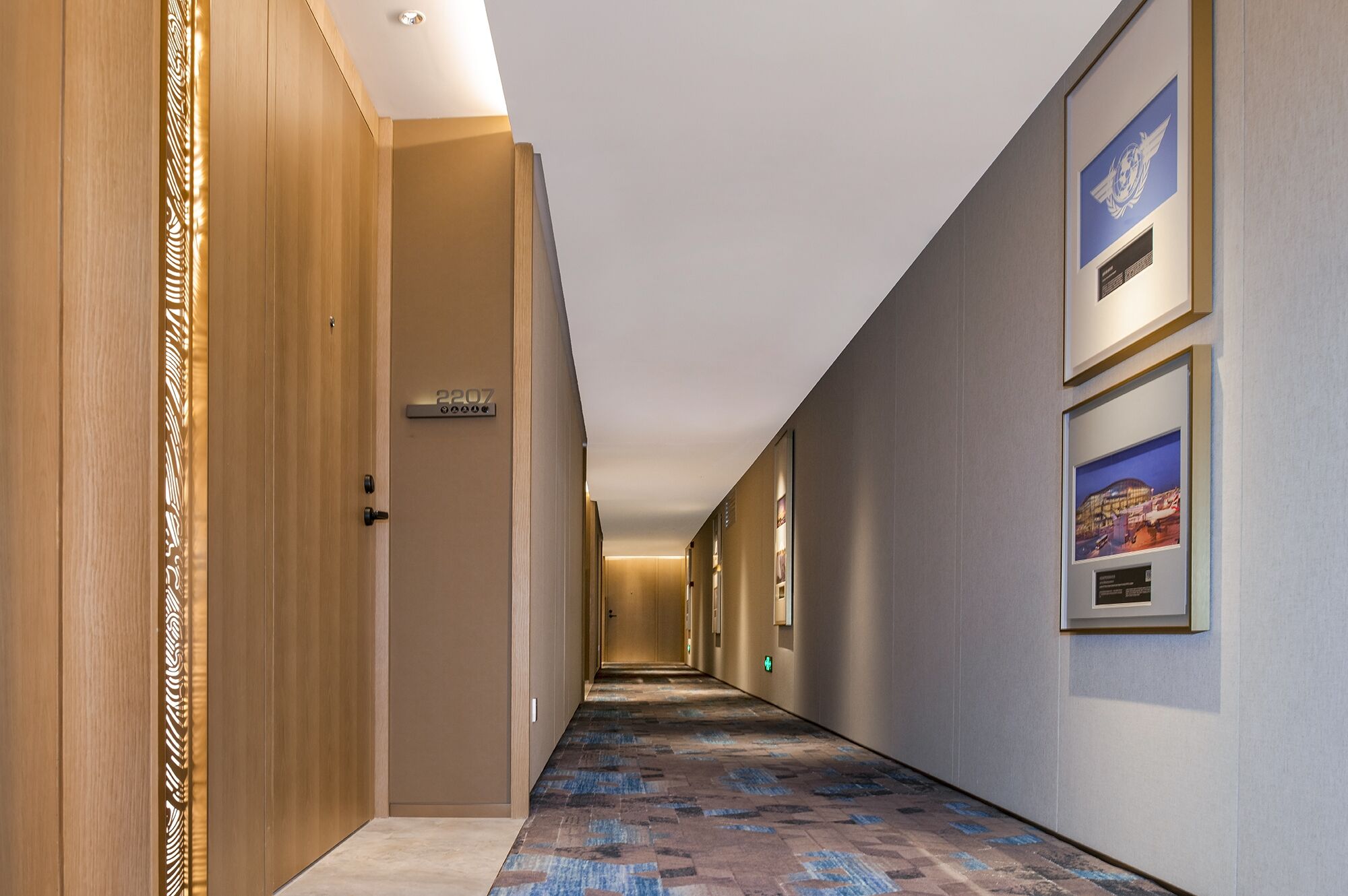 A hotel hallway with a carpeted floor, wooden doors, and framed pictures on the walls.