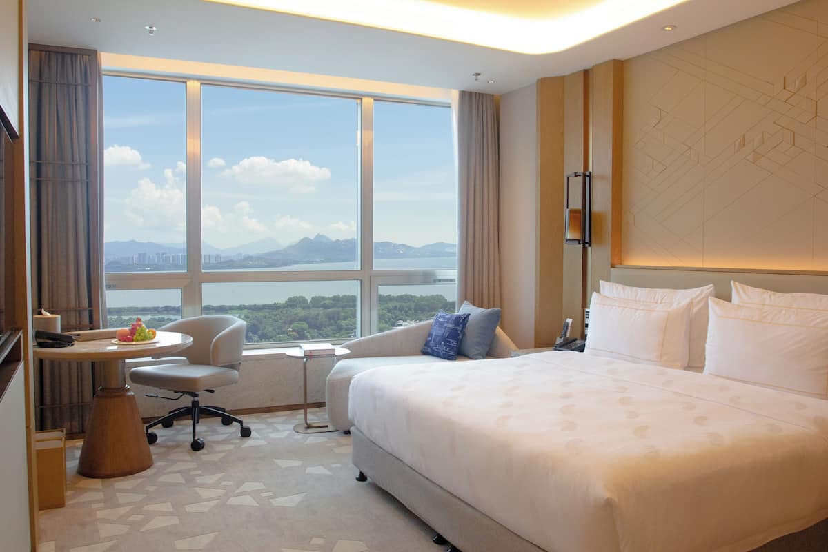 Une chambre d’hôtel avec un grand lit, un bureau, une chaise et une vue sur un plan d’eau et des montagnes.