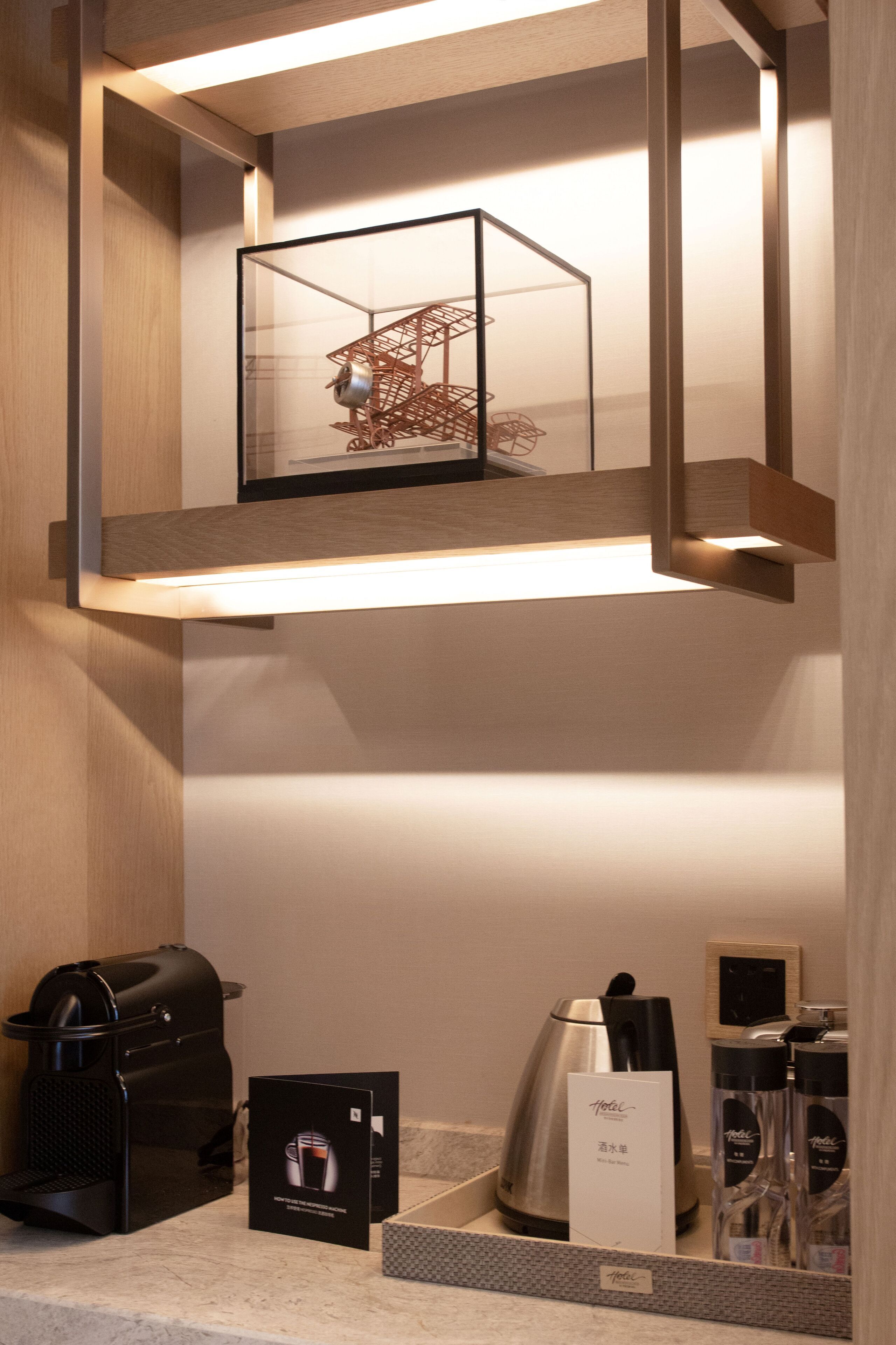 A hotel room with a coffee maker, a kettle, and a glass display cabinet with a decorative item.