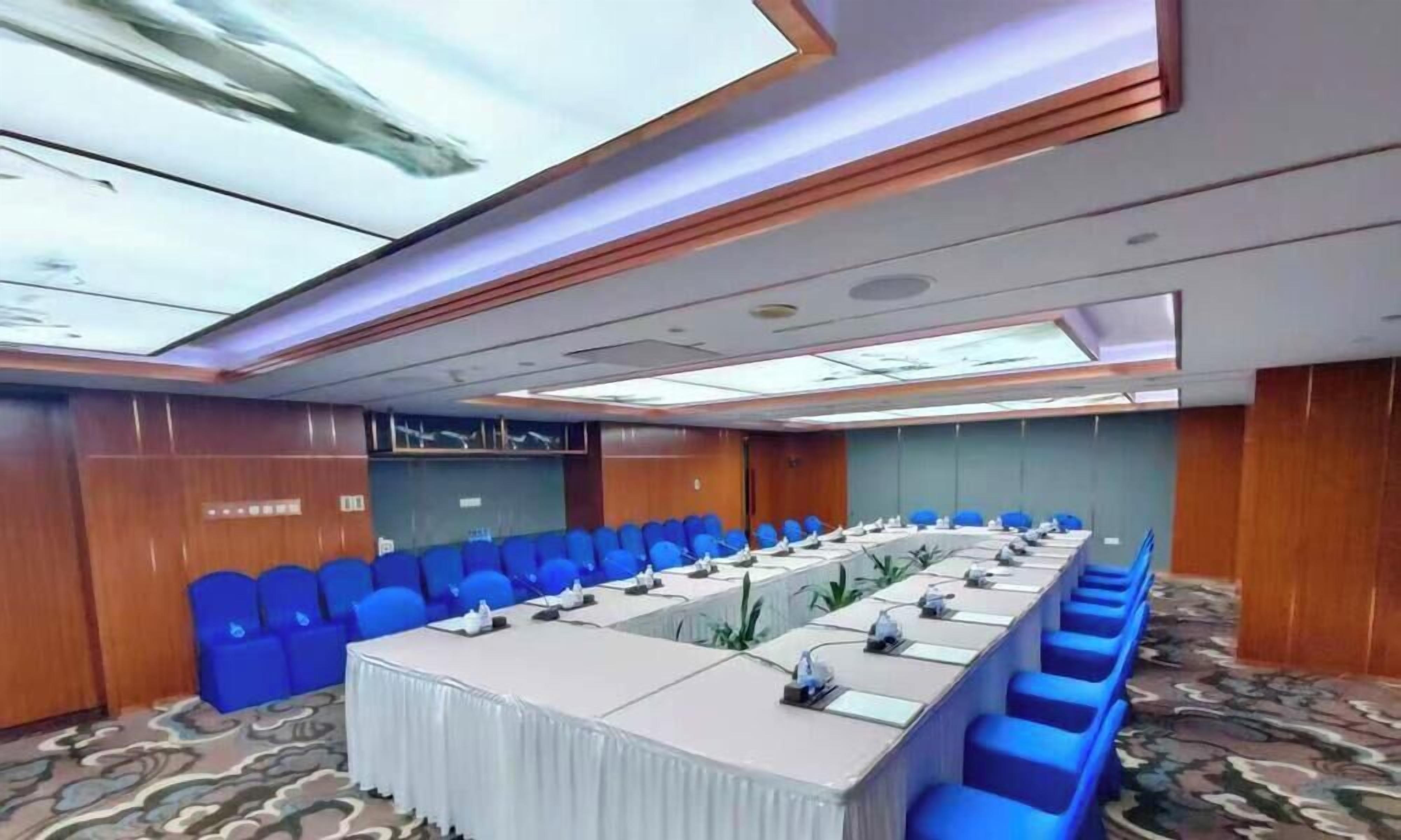 A conference room with a long table, blue chairs, and a patterned carpet.