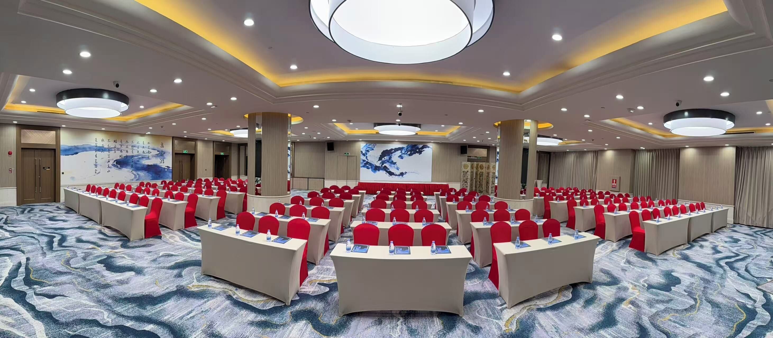 Un salón de conferencias con mesas redondas, sillas rojas y una pantalla grande.